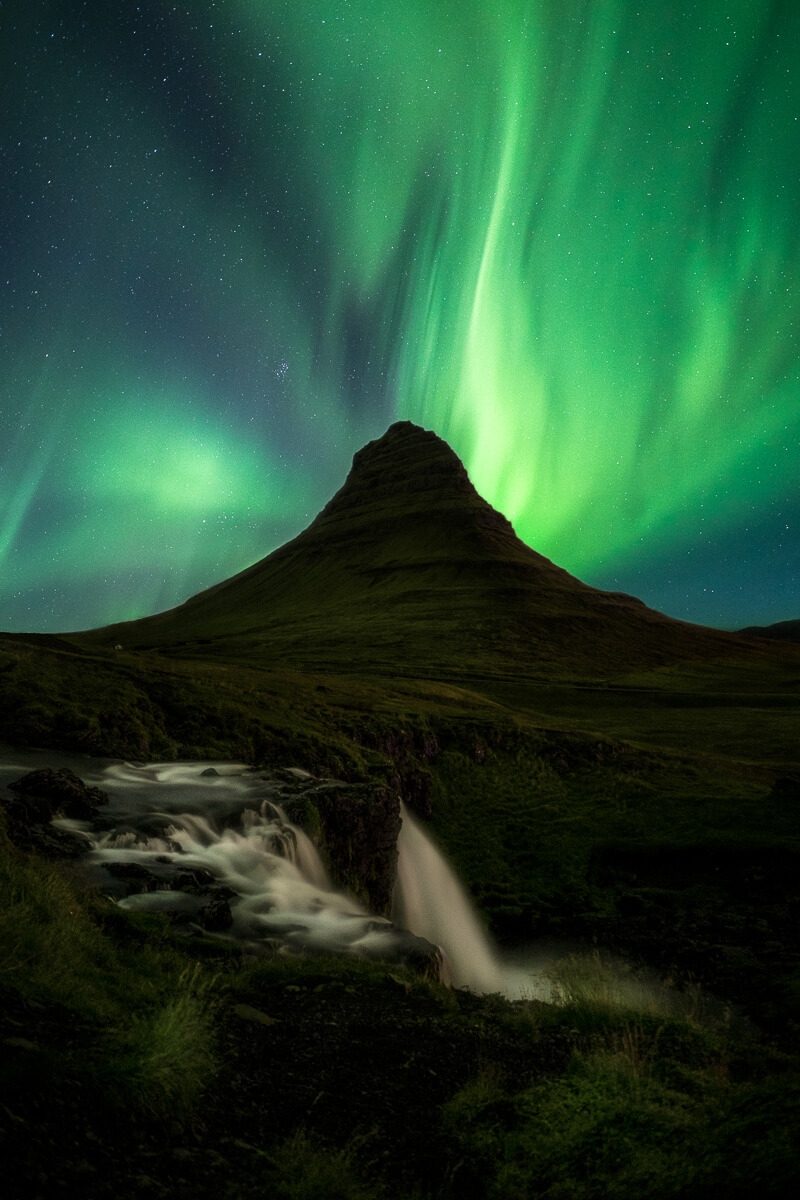 Northern lights dance behind Kirkjufell and kirkjufellsfoss