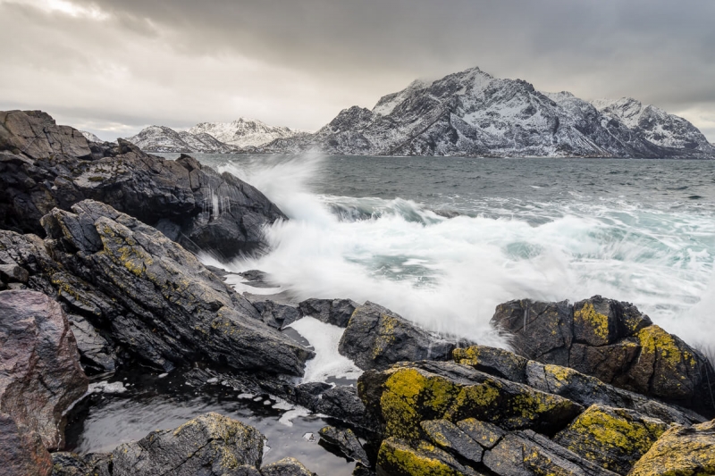 rough seas crashing against rocks, mountains in the distance
