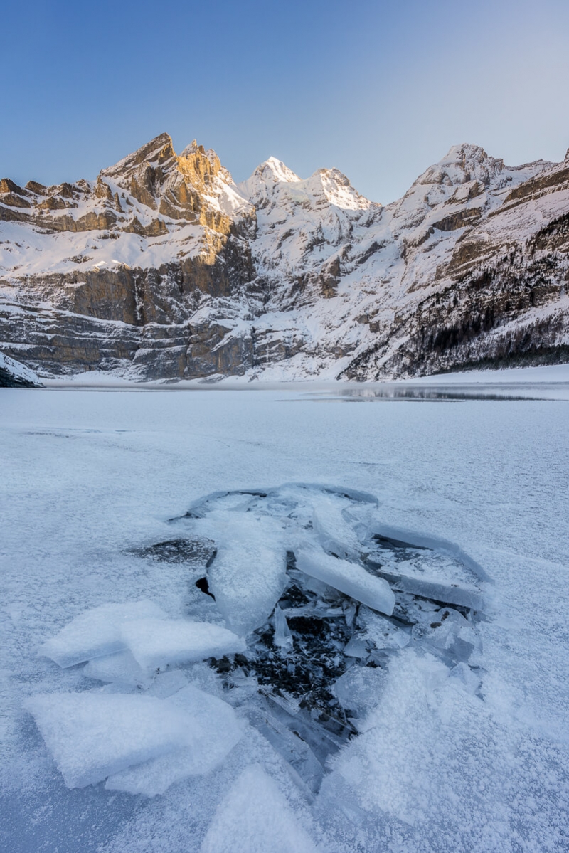 Cracked ice on frozen lake wit sunlight mountains